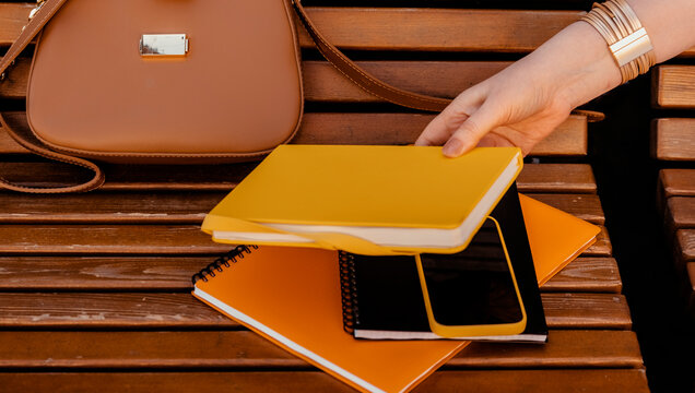 Woman puts yellow notebook on wooden street bench. Education organization time management strategy concept.