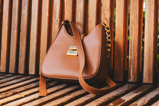 Fashionable brown leather woman handbag rests on wooden bench. Modern stylish casual accessory fashion luxury lifestyle concept.