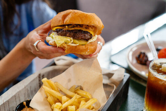 Woman holding big juicy beef burger over french fries basket