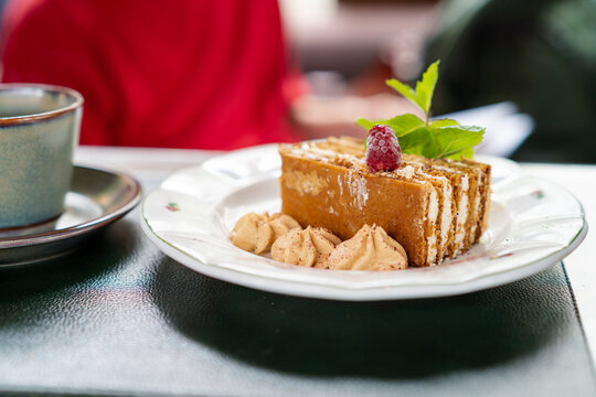 Layered honey cake slice with mint and coffee cup on cafe table