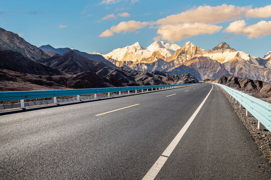 Empty asphalt road leading to majestic snow capped mountains under blue sky