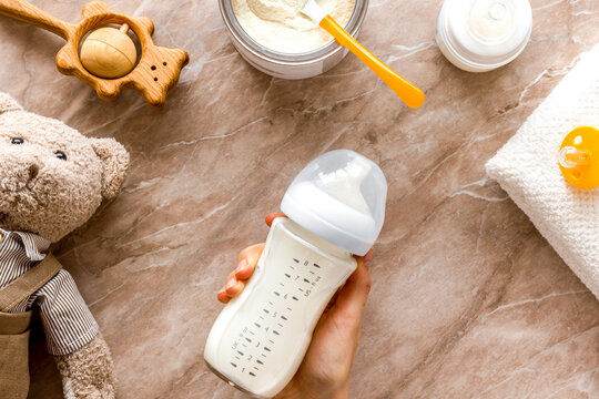 Milk bottle for feed baby in hands near toys and accessories on brown background top view pattern