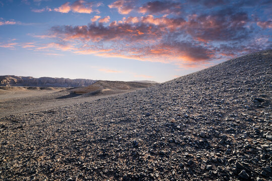 A stony desert landscape with yardang landforms under a dramatic sunset sky in Dahaidao, Xinjiang, China