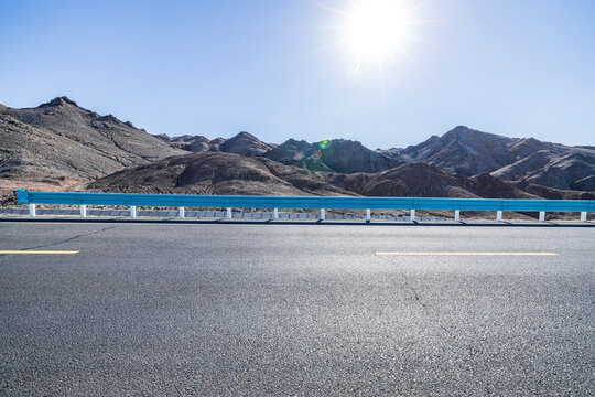 An empty asphalt road through a mountainous desert landscape under a blue sky in Qinghai, China