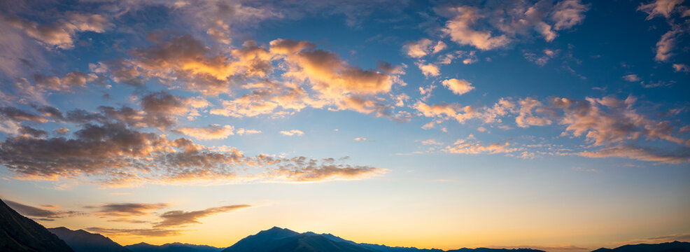 Golden sunset sky with clouds over silhouette of mountains in the background