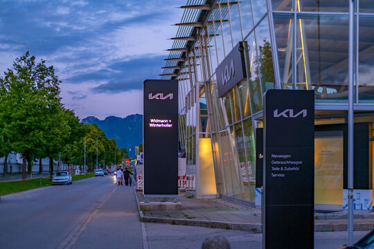 Kia dealership exterior corporate logos modern facade at dusk, European automotive retail center, mobility business car sales, global manufacturer branding, electric vehicle showroom F&uuml;ssen, Germany