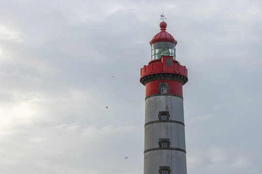 View of the Pointe Saint-Mathieu lighthouse with its distinctive red lantern and white tower against a cloudy sky in Plougonvelin, Brittany, France.