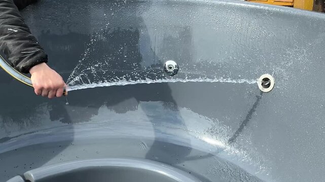 jacuzzi washing process with strong water stream removing dirt from tub walls, jacuzzi interior getting cleaned with spray, foam dissolving on surface, outdoor setting, sanitation and care concept