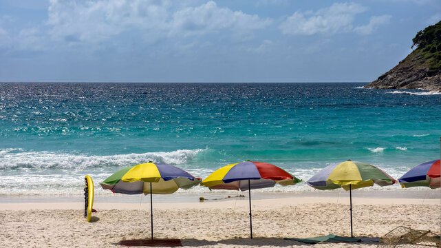 View of colorful beach umbrellas on the white sand of Ko Racha Yai with turquoise sea and rocky headland in the background in Phuket, Phuket, Thailand.