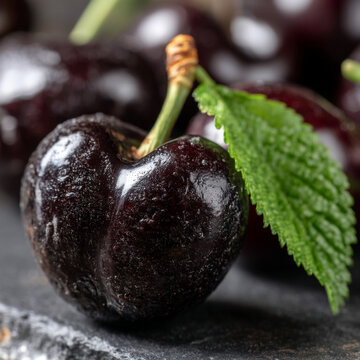 Macro view of a ripe dark black cherry with a green leaf and textured skin, nutrition