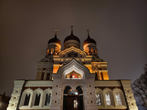 Symmetrical low angle night view of illuminated facade and onion domes of Alexander Nevsky Cathedral in Tallinn, Estonia.