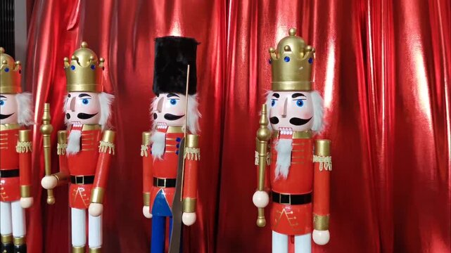 Row of wooden nutcracker soldiers in red uniforms with gold crowns standing against red curtain backdrop. Traditional Christmas decorations for winter holiday and ballet concept.
