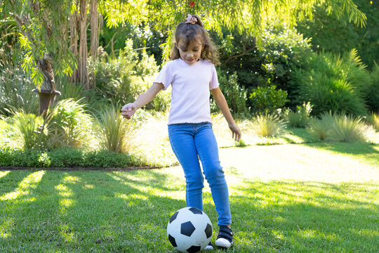 African American child standing on lawn focusing on soccer ball by planter with pink scrunchie