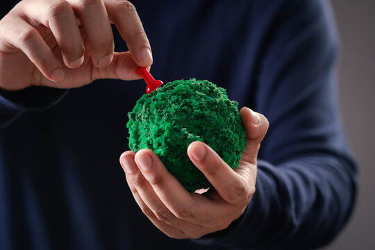 Close-up of a hand placing a red push pin on a green globe model, symbolizing global location, environmental planning, sustainable development, destination strategy, mapping, and business expansion.