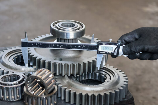 Mechanic measuring the outer diameter of an industrial gear using a digital caliper.