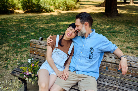Affectionate Couple Sitting on Park Bench &mdash; Asian Woman Leaning on Partner in Summer Romance