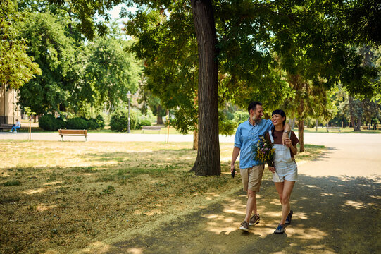 Happy Couple Including Asian Woman Walking in Urban Park on a Summer Day with Flowers
