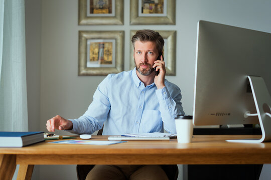 Confident middle-aged man using his computer at home and having a business call