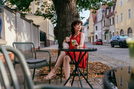 Stylish Mature Woman Drinking Iced Matcha at Outdoor Cafe in European City
