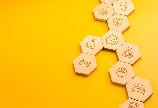Wellness and longevity concept with healthy lifestyle icons on wood hex blocks, featuring nutrition, fitness, meditation, preventive healthcare, lifestyle medicine, self care, and holistic health.