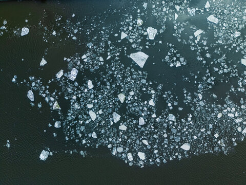 Aerial view of fragmented river ice floating on dark winter water surface.