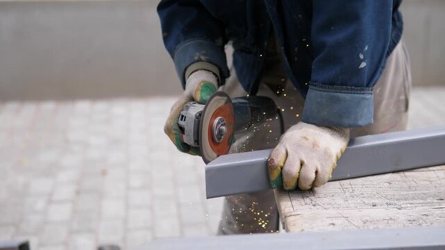 A focused and industrious worker is cutting a metal bar with a grinder on an outdoor construction site. The scene captures the detailed action of the worker's hands and tools, emphasizing.