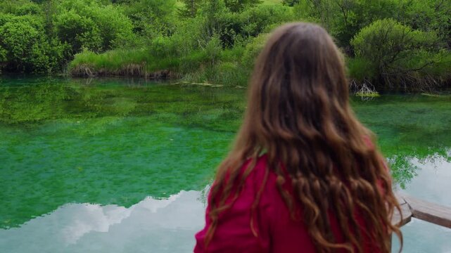 Female Tourist Looks Across The Tranquil Lake At Zelenci Nature Reserve In Slovenia. Close-up Medium Shot