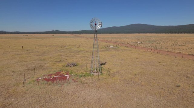 Drone orbits windmill with golden grassland and mountain backdrop, remote northern Lassen County, California.