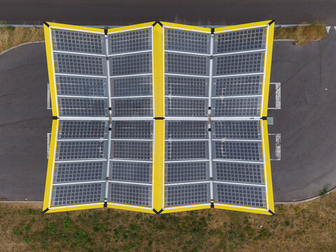 Diepenbeek, Belgium - 04 August 2026: Aerial view of a solar panel canopy for electric vehicle charging with bright yellow frames and dark photovoltaic panels on an asphalt surface.