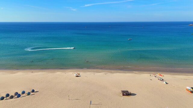 A Dynamic aerial view of people enjoying watersports like jetskiing, swimming, and relaxing on a tropical beach in Vietnam. Sunny daylight.