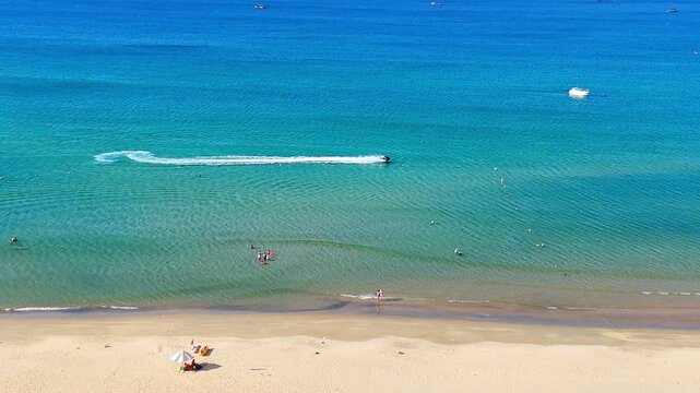 A Dynamic aerial view of people enjoying watersports like jetskiing, swimming, and relaxing on a tropical beach in Vietnam. Sunny daylight.
