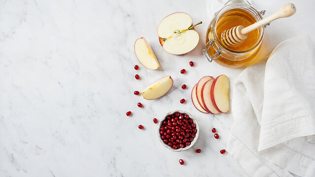 Glass jar of honey with wooden dipper and apple slices on marble