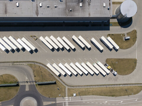 Poland - 09 August 2026: Aerial view of the Action logistics hub featuring rows of white semi-trailers parked in a large paved lot next to a warehouse and storage tank.