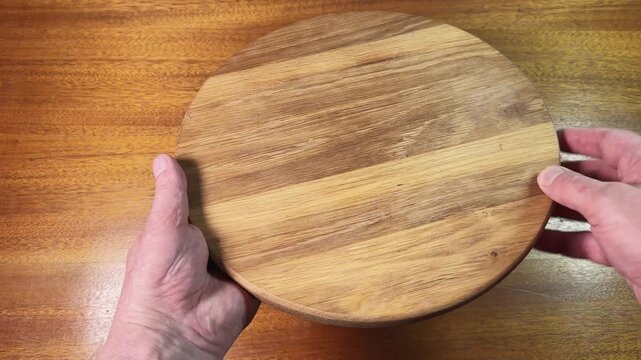 Round oak cutting board in hands above the wooden table