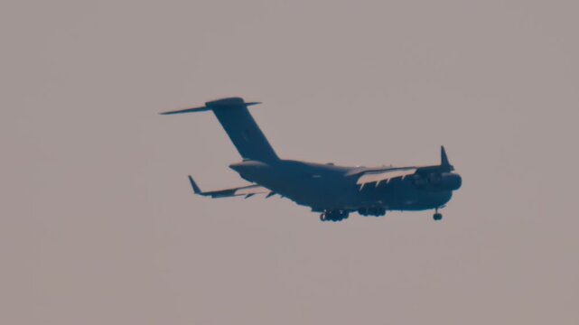 Military transport aircraft landing on runway during sunset.