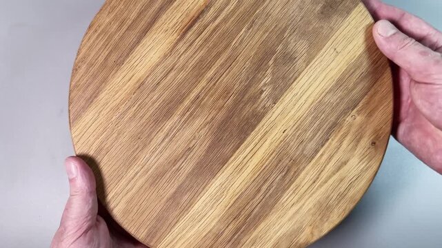 Round oak cutting board in hands on a gray background