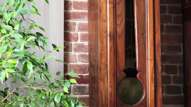 Antique longcase floor clock in wooden case against brick wall
