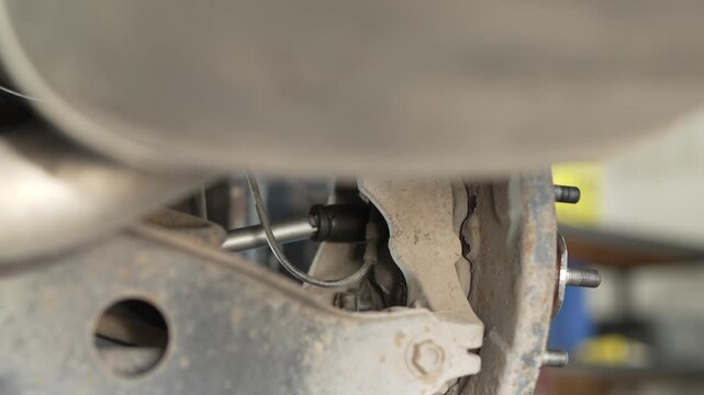 A mechanic using a socket wrench behind a car wheel.