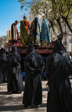 A Holy Week procession in Spain featuring a local religious brotherhood with hooded penitents and a float bearing religious images, which has been designated a site of international tourist interest.