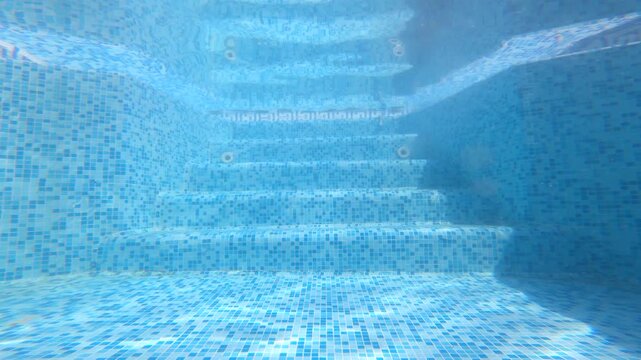 Underwater view of empty blue swimming pool steps with crystal clear water and mosaic tiles.