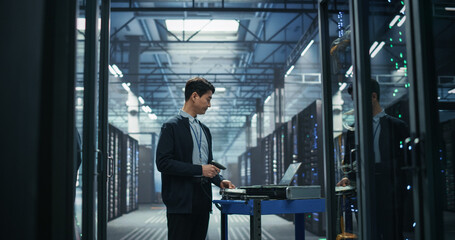 Fototapeta premium Asian Male Network Technician Uses Handheld Barcode Reader to Register New Server Hardware on Mobile Cart Beside Laptop, Performing Inventory Audit and Equipment Provisioning in AI Data Center.