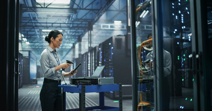 Asian Female It Technician Using Handheld Barcode Scanner to Register Server Component for Hardware Inventory Tracking, Working at Maintenance Cart With Laptop Computer in AI Data Center Facility.