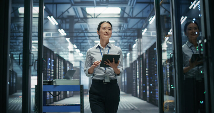 Portrait of Asian Female Cloud Engineer Using Digital Tablet Computer While Walking Between Rack Rows, Hardware Inspection and Capacity Planning Checks in High Performance AI Colocation Data Center.