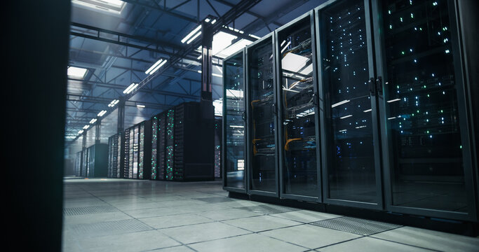 Low Angle Wide Shot of AI Data Center Interior: Rows of Server Rack Cabinets With Fiber Optic Cabling and Raised Floor Ventilation Grilles Supporting Cloud Storage and Machine Learning