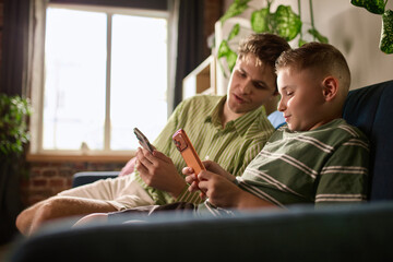 Boy and young man comparing phones during money transfer lesson. Concept of supervised payments for parental controls and youth banking services.