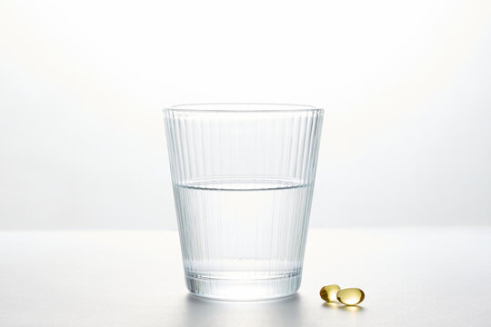 Glass of fresh water with dietary supplement capsules on white background