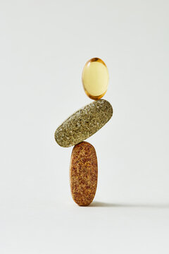 Balanced stack of vitamin capsules and herbal supplement pills on neutral background