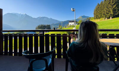 Fototapeta premium cozy wooden balcony with comfortable lounge chair overlooking scenic green mountains