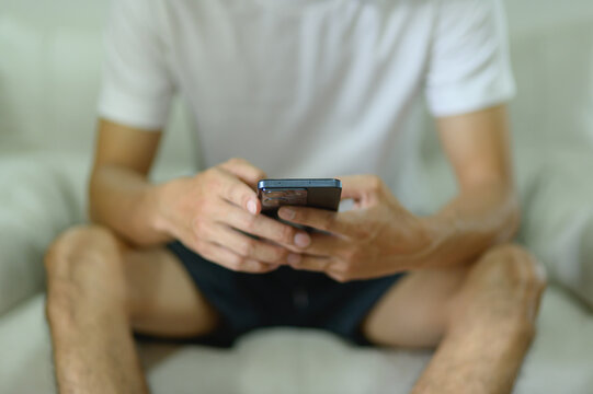 Young Man Sitting on Couch Using Smartphone with Focus on Hands and Device