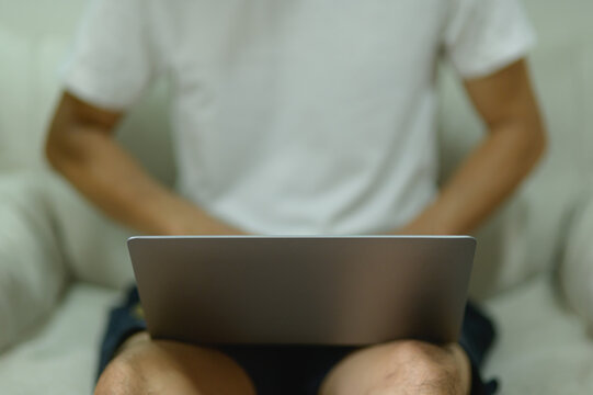 Man sitting with legs apart using laptop at home, casual relaxed work setting